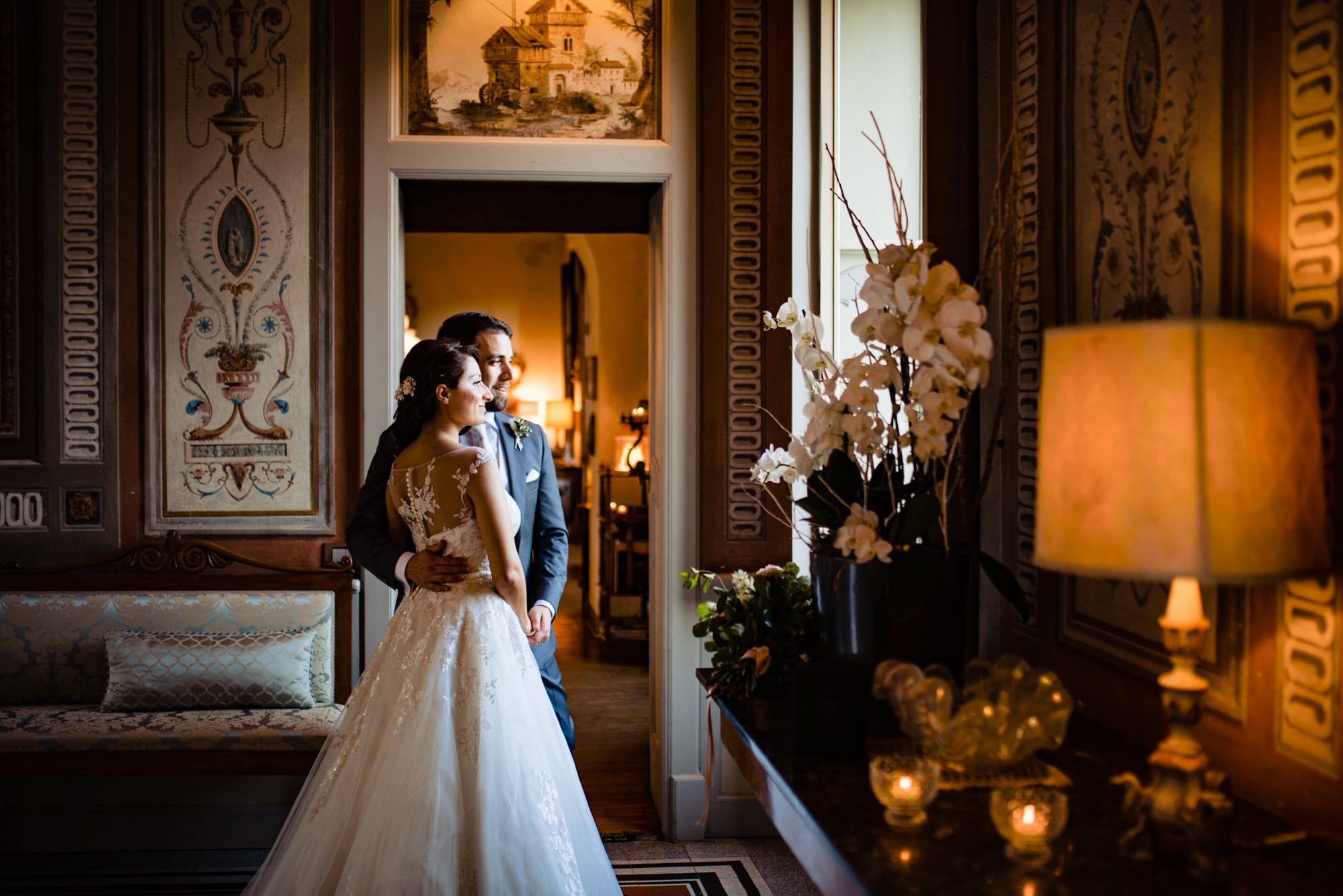 Sposi abbracciati all'interno di Villa Bossi, avvolti da luce naturale proveniente da una finestra. Reportage elegante di un matrimonio romantico.