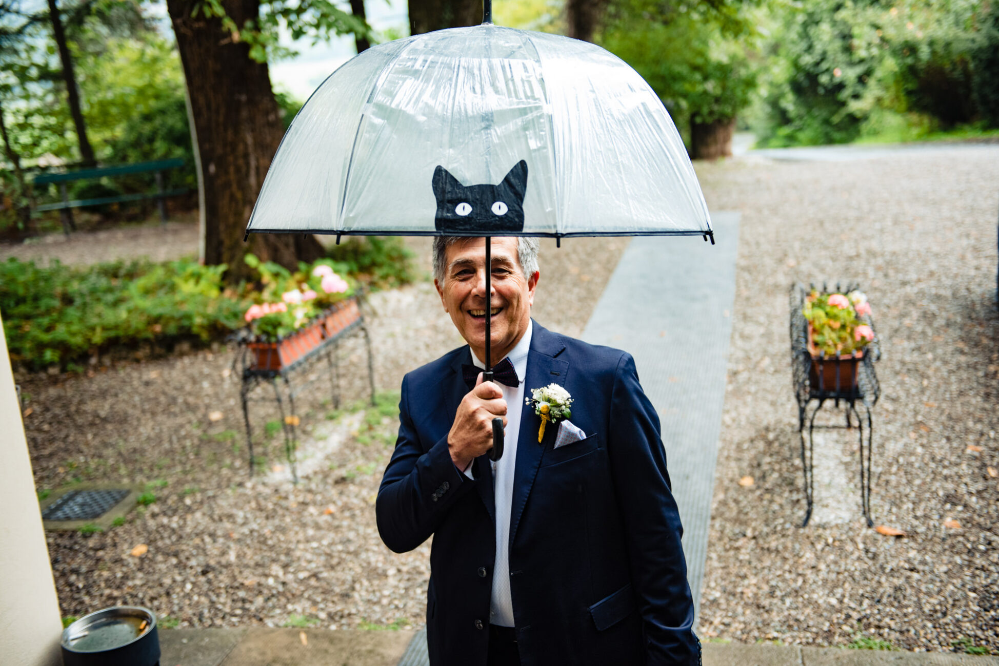 Il padre dello sposo tiene un ombrello, pronto per qualsiasi imprevisto meteo. Fotografia scattata da Paolo Lamperti Fotografo Matrimonio Varese al Castello di Tabiano.